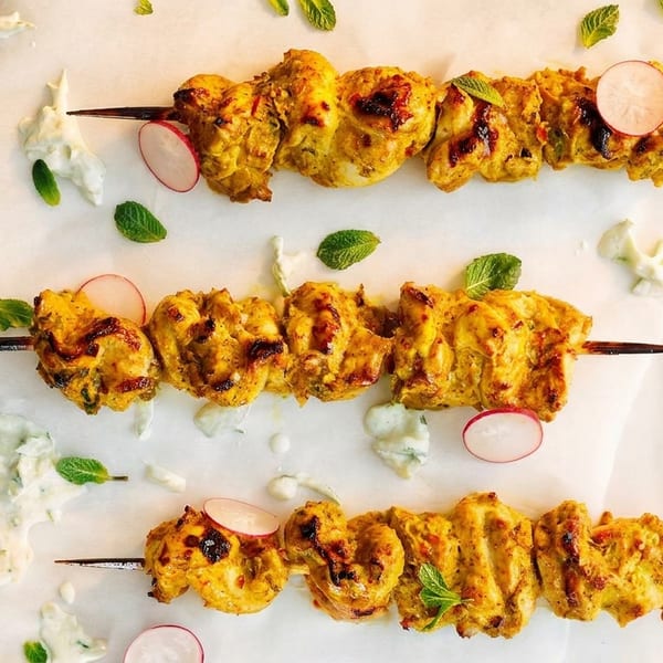 Three skewers of golden chicken tikka, garnished with radish slices, mint, and creamy sauce.