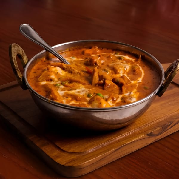 Indian butter chicken or paneer curry in a metal bowl with a spoon on a wooden board.