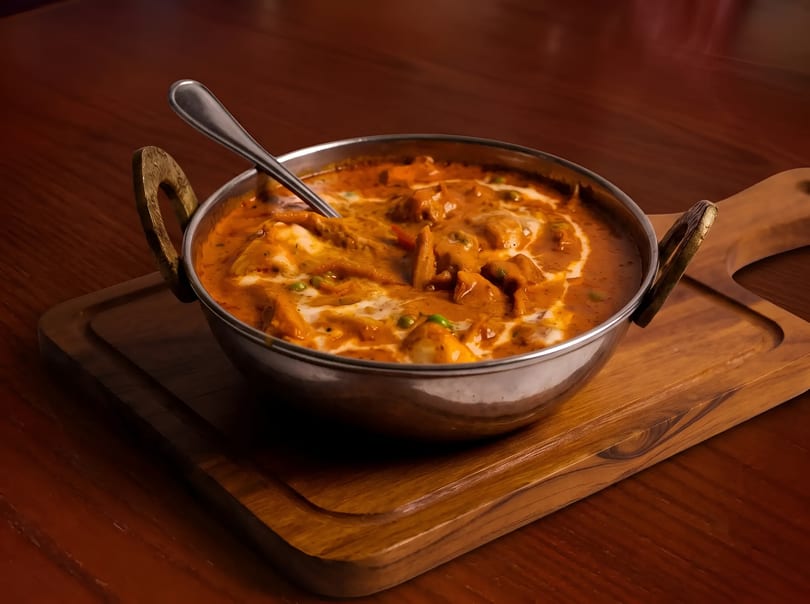 Indian butter chicken or paneer curry in a metal bowl with a spoon on a wooden board.
