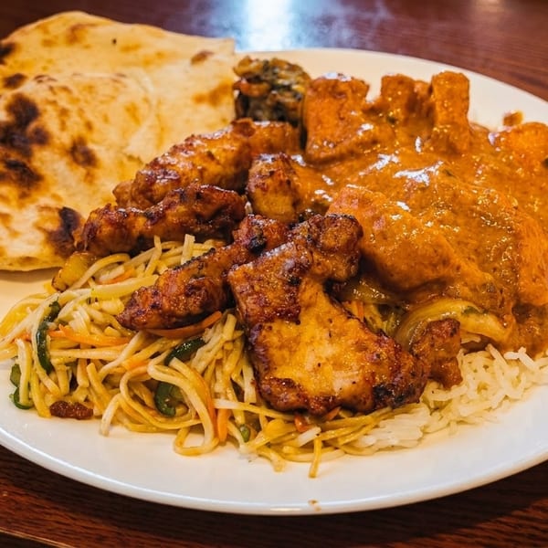 A white plate filled with Indian food, including naan, chicken tikka masala, noodles, and rice.