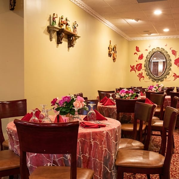 Restaurant dining room with tables set with red tablecloths, floral centerpieces, and dark wood chairs.