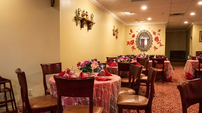 Restaurant dining room with tables set with red tablecloths, floral centerpieces, and dark wood chairs.