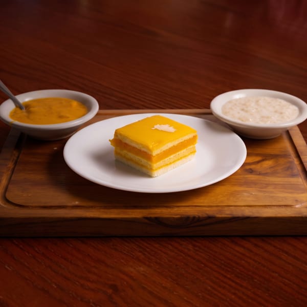 A mango cake slice with two small bowls of sauces on a wooden board.