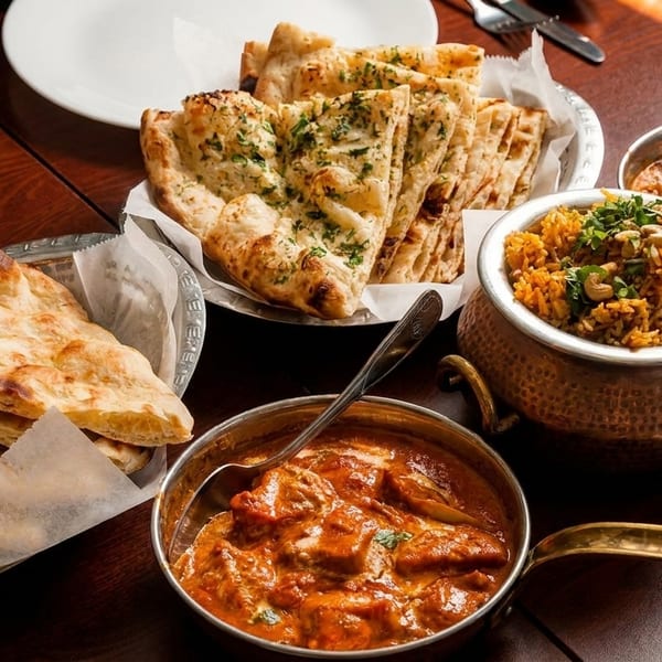 Indian feast with naan bread, rice, and two bowls of curry on a wooden table.