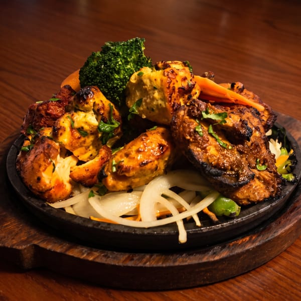 Sizzling platter of grilled chicken, broccoli, and onions on a dark wooden table.