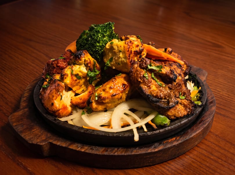 Sizzling platter of grilled chicken, broccoli, and onions on a dark wooden table.