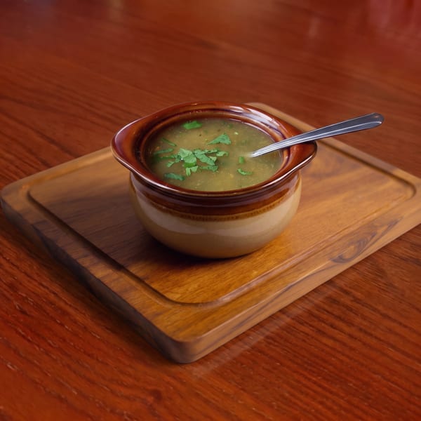 Hearty soup with fresh herbs in a ceramic bowl on a wooden board and table.