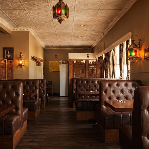Empty restaurant interior with brown leather booths, dark wood tables, and ornate Moroccan-style lanterns.