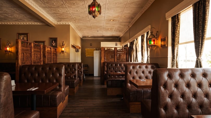 Empty restaurant interior with brown leather booths, dark wood tables, and ornate Moroccan-style lanterns.